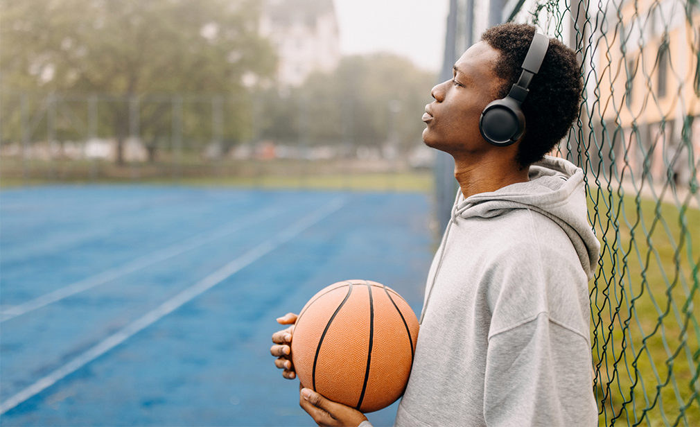 Young person listening to music with basketball outside.