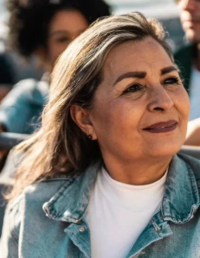A woman with long gray hair sits on an open-air bus, gazing into the distance.